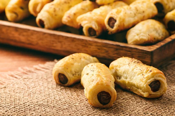 Puff pastry sausage rolls on brown wooden background.