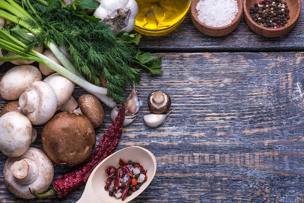 Mushrooms, parsley, dill, onion, olive oil, spices - ingredients for the preparation of mushroom dishes in a frying pan on a wooden background