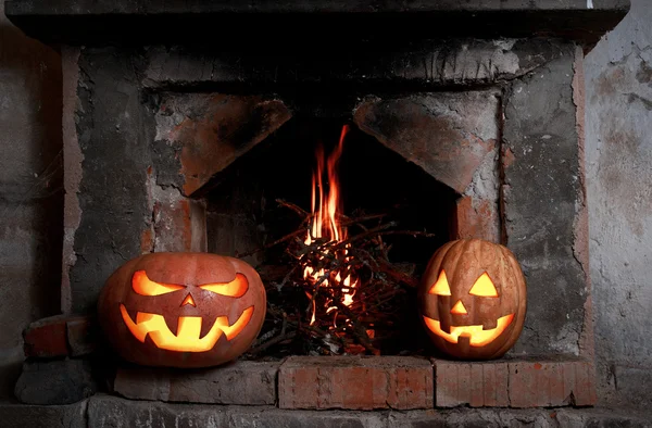 Two Halloween pumpkins at the fireplace with fire