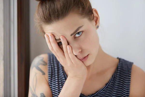 Beautiful portrait of bored female resting half of her face on her palm. Attractive girl with brown hair and blue eyes getting tired of wonky conversation, trying to hide from dull talk under her arm.