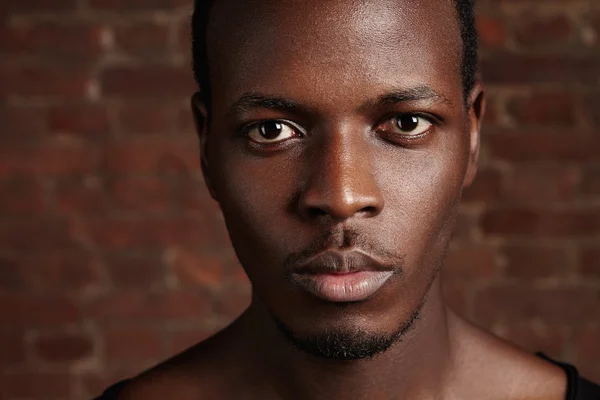 Beauty and skin care. Highly-detailed close up portrait of good-looking dark-skinned young man with clean healthy glowing skin, looking at camera with serious confident expression, posing in studio