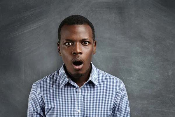 People and education concept. Portrait of handsome African student with bugged eyes and mouth wide open, looking surprised and shocked with new topic during lesson in physics, standing at chalkboard