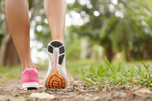 Outdoor activity and sports. Freeze action closeup of pink running shoes against green grass background. Woman jogger exercising in park or forest, getting prepared for marathon. Focus on right sole