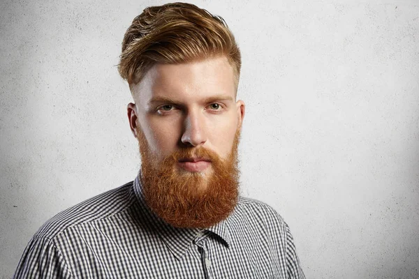 Style and fashion concept. Courageous attractive young model dressed in checkered shirt posing indoors after visiting hairdresser or barber demonstrating his stylish haircut and well-trimmed beard