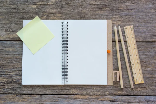 Open notebook on wooden background with pencils and ruler.