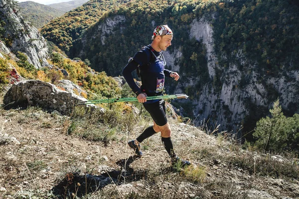 Young male runner with walking poles running through steep cliff