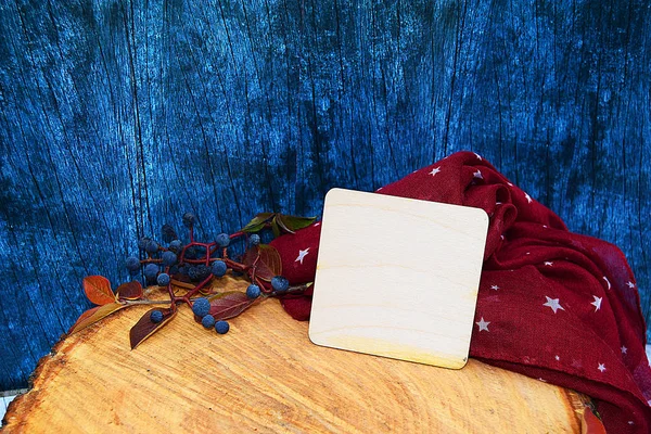 Warm burgundy gloves with a scarf and hat on wood background blue color with autumn leaves, and cut down a tree