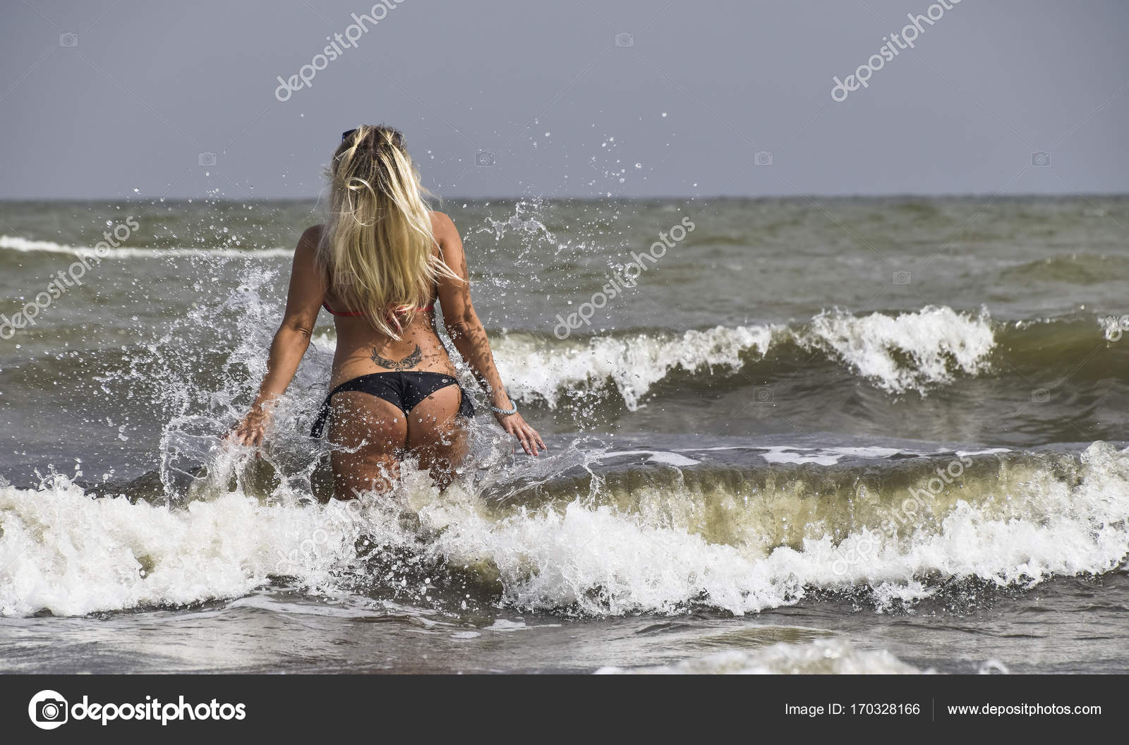 Обнаженная блондинка с длинными желтыми бусами купается в море