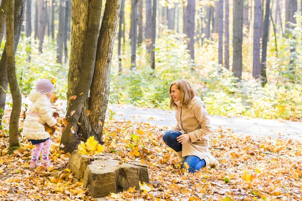 Happy family mother and child girl playing throw leaves in autumn park outdoors