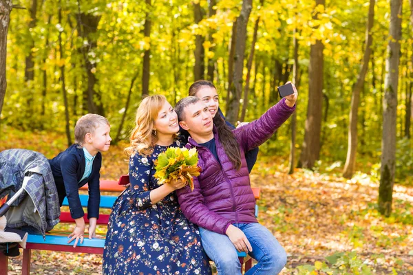 Family, childhood, season, technology and people concept - happy family photographing in autumn park