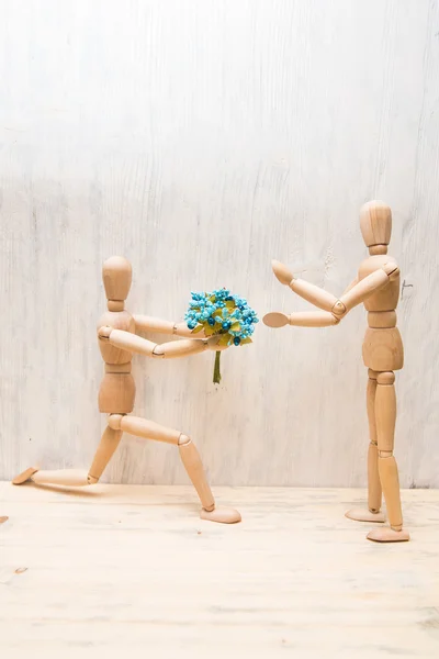 The wooden little man gives flowers to the girl