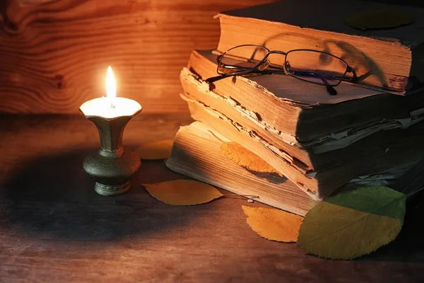 Old tattered book on a wooden table lighted candle and glasses