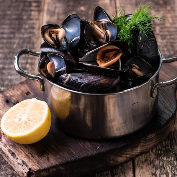 Mussels in copper cooking dish and lemon on dark wooden background