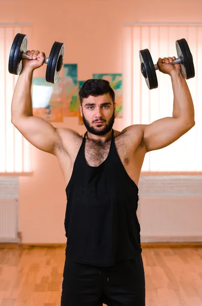 Handsome young muscular man exercising with dumbbells.