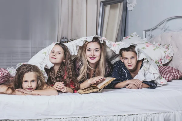 One big happy family. Mom reads a book to their children in bed.