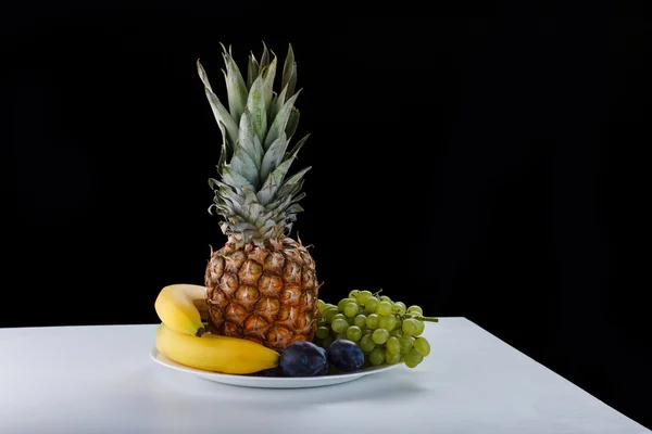 Fruits on a black background. Bananas, plums, pineapple, grapes