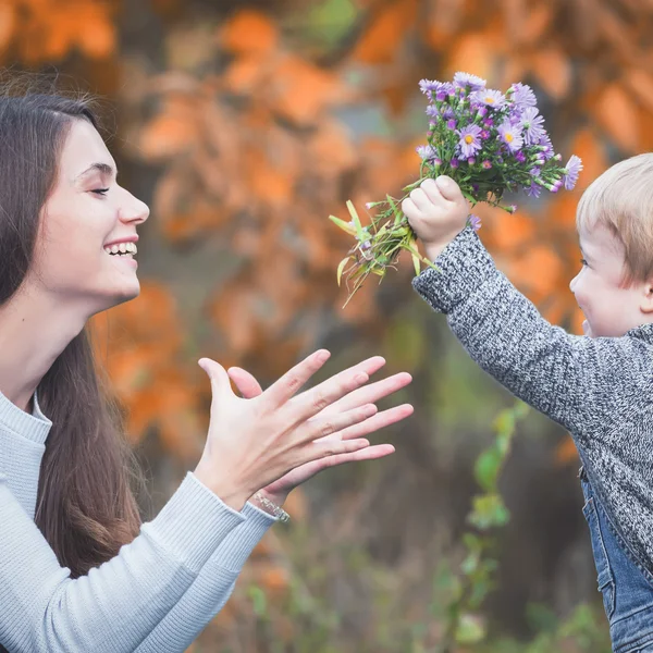 Child gives to happy mother flowers. Fall colors background