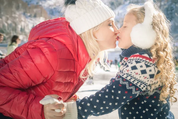 Happy mother and daughter kissing outdoor, ice skating