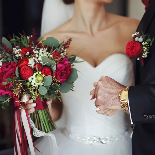 Bride holds bouquet in one arm and fiance\'s hand in another