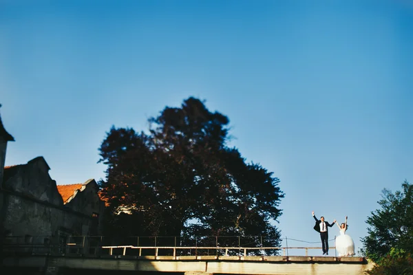 Bride and goom jump behind an old castle on bright summer day