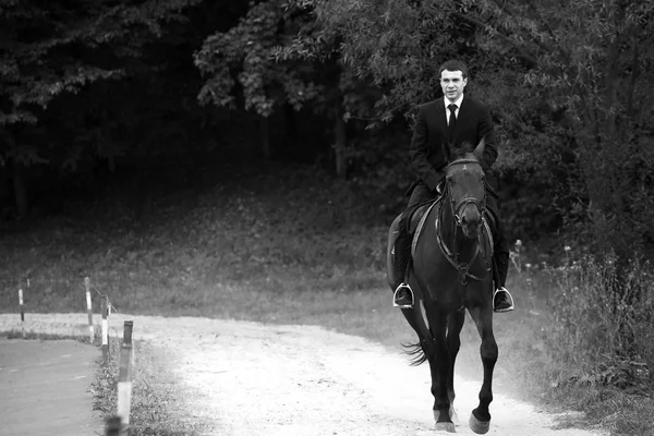 Man in black suit rides a horse