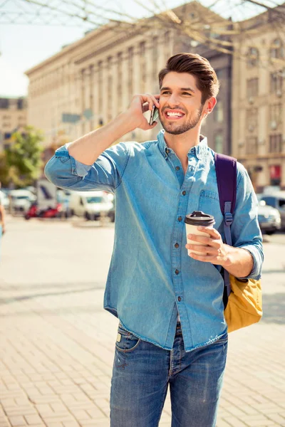 Handsome smiling tourist with cup of coffee talking on phone