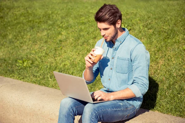 Handsome guy drinking juice and working on laptop in the park