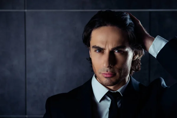 Handsome brutal man in black suit combing hair with fingers
