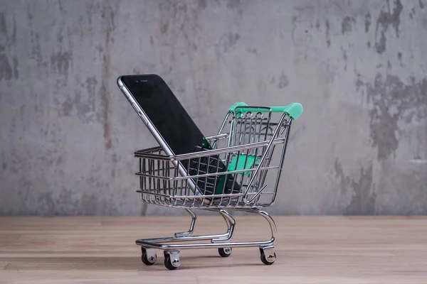 Shopping cart with smart phone inside, on the wooden table