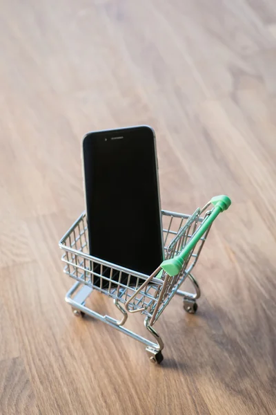 Shopping cart with smart phone inside, on the wooden table