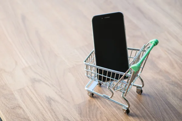 Shopping cart with smart phone inside, on the wooden table