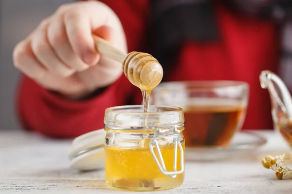 Man hold cup of hot tea in glass cup, jar of honey, honey dipper