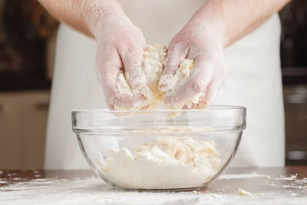 Hands of man preparing mound of bread dough on clear black table