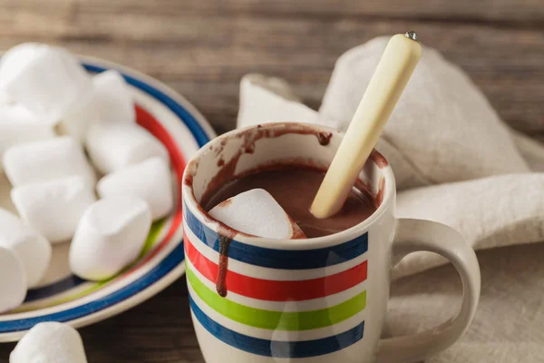 Cups of hot cocoa with marshmallows and cinnamon sticks on woode