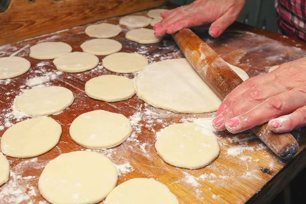 Woman making ukrainian dumplings or varenyky, roll out the dough of rolling pin