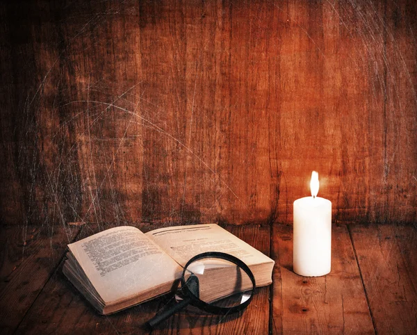 Open book and a white candle on a wooden table. Reading by candlelight. Vintage composition. Free space for text. Ancient library. Antique literature.