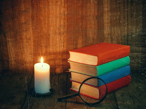Books and a white candle on a wooden table. Reading by candlelight. Vintage composition. Free space for text. Ancient library. Antique literature.