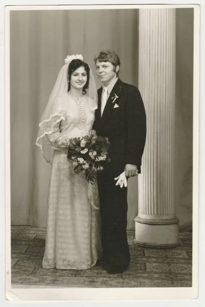 Vintage photo shows a bride with bridegroom. Bride wears  a soft veil and holds wedding flowers (bouquet) . Retro black & white  photography.