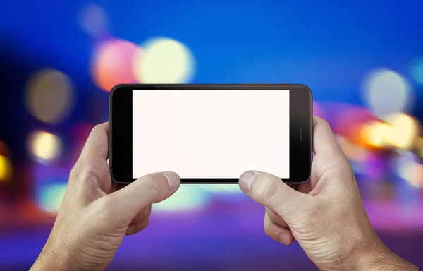 Use camera or play game on mobile phone with isolated display mockup. Phone in hands, horizontal position. City, night lights in background.