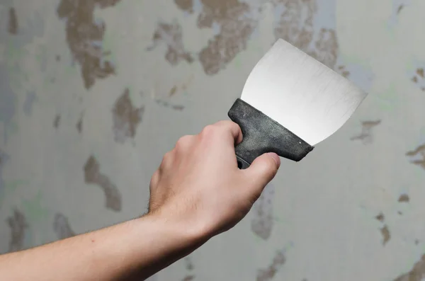 Trowel in man\'s hand. Tool for getting rid of the wallpaper