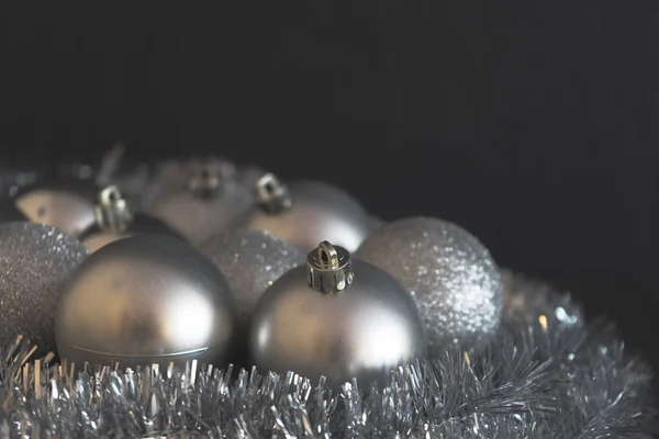 Vintage low contrast photo of shiny and bright silver christmas balls decoration lying on silver christmas chain on dark black backdrop in soft focus.