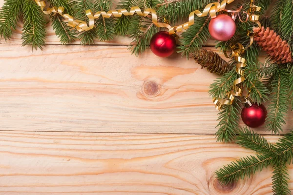 Corner frame of fir branches with Christmas decorations on a light wooden background