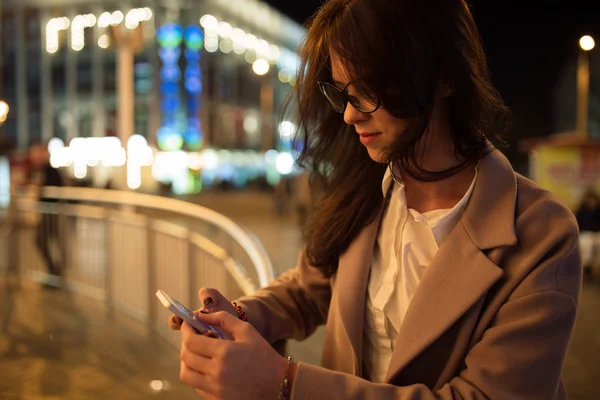 Woman holding a smartphone looking to screen in city night - technology, communication concept