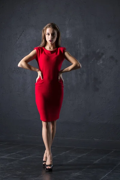 Lady in red dress posing against textured wall background