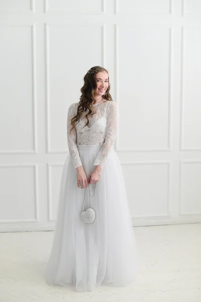 Bride standing with wedding accessories in white room.