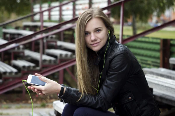 Young beautiful girl look and listening music on your mobile phone  the old stadiums bench