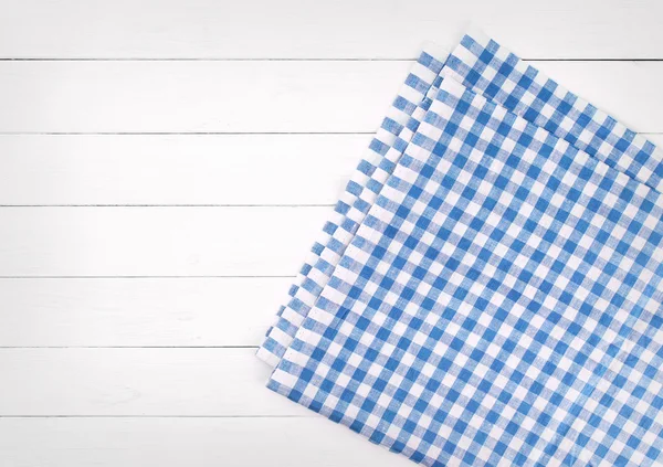 Blue checkered folded tablecloth on white wooden table, top view