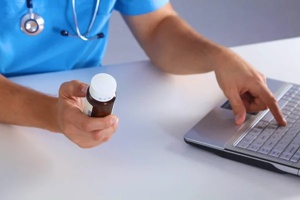 Male medicine doctor hands hold jar of pills and type something on laptop computer keyboard. Panacea life save, prescribing treatment, legal drug store, take stock, consumption statistics concept