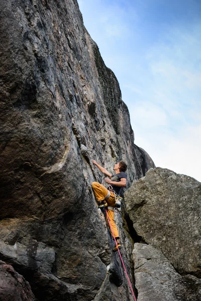 Young man lead climbing a rock, wearing climbing equipment, outdoors.