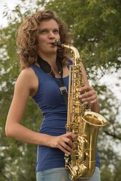 Beautiful girl with curly hair playing the saxophone in gold on